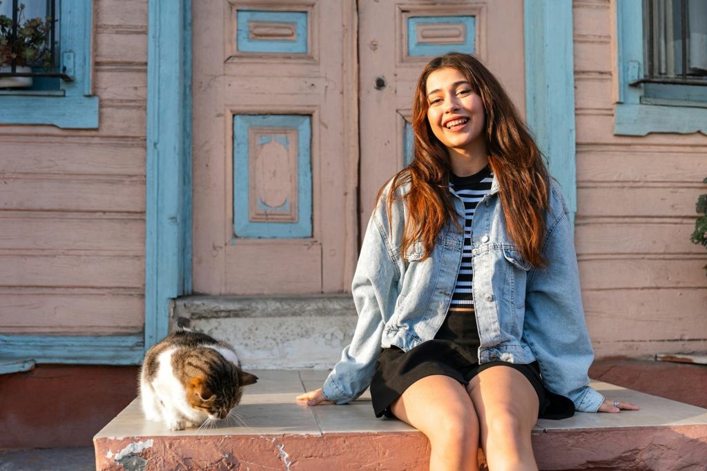 A cheerful young woman sitting on a porch with a cat, enjoying the sunny day.