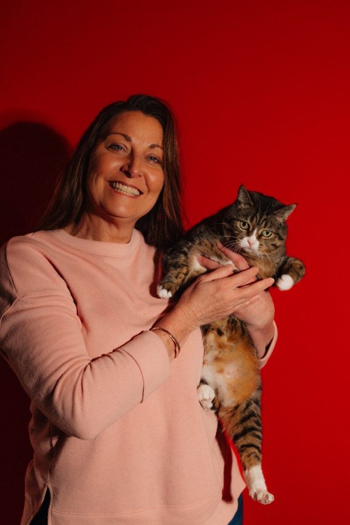 Woman holding a tabby cat against red background