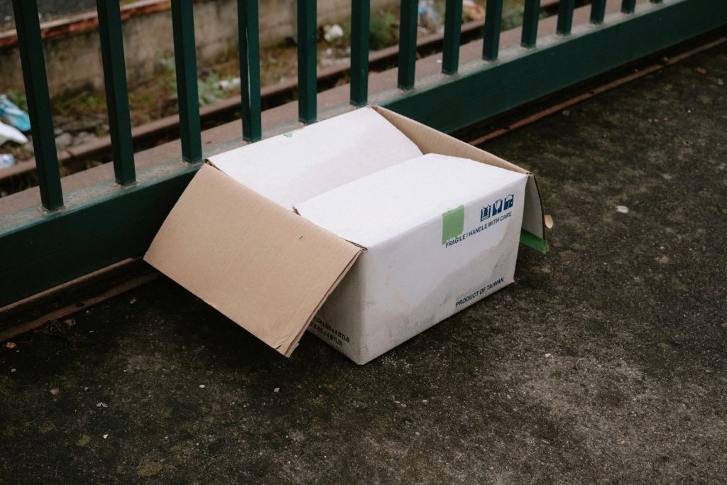 Abandoned cardboard box by railing on a gritty concrete surface in urban environment.
