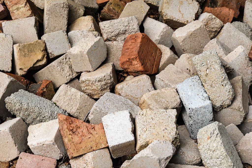 A detailed view of a rough, textured pile of concrete and clay bricks in various colors.
