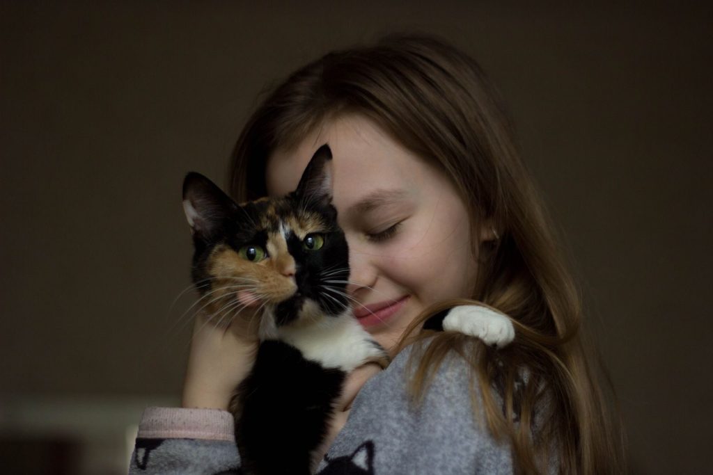 Smiling little girl with closed eyes cuddling adorable three colored cat with green eyes