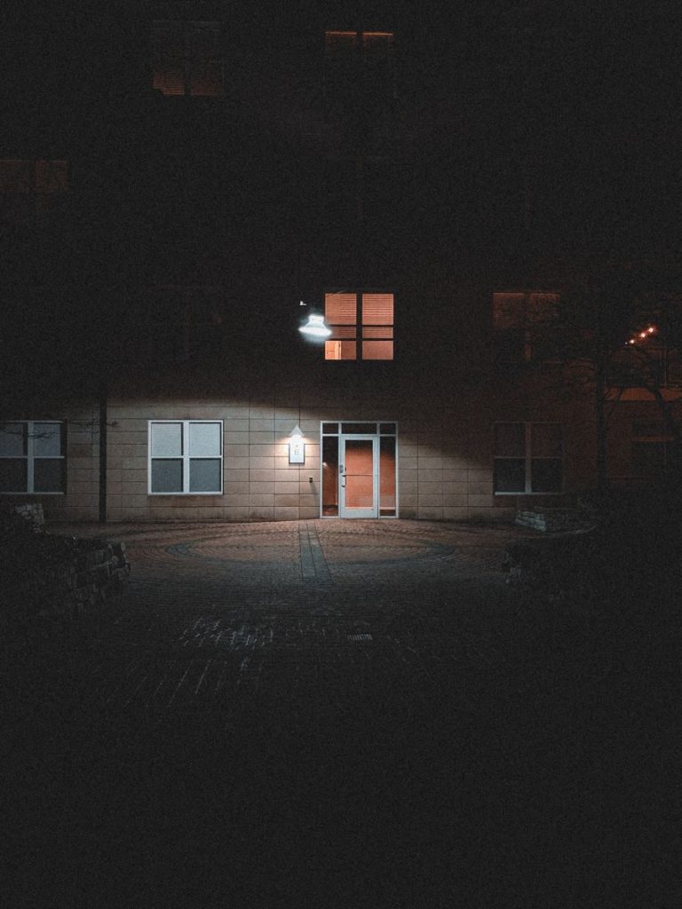 A dimly lit building exterior at night showcasing a glowing entrance and subtle architectural features.