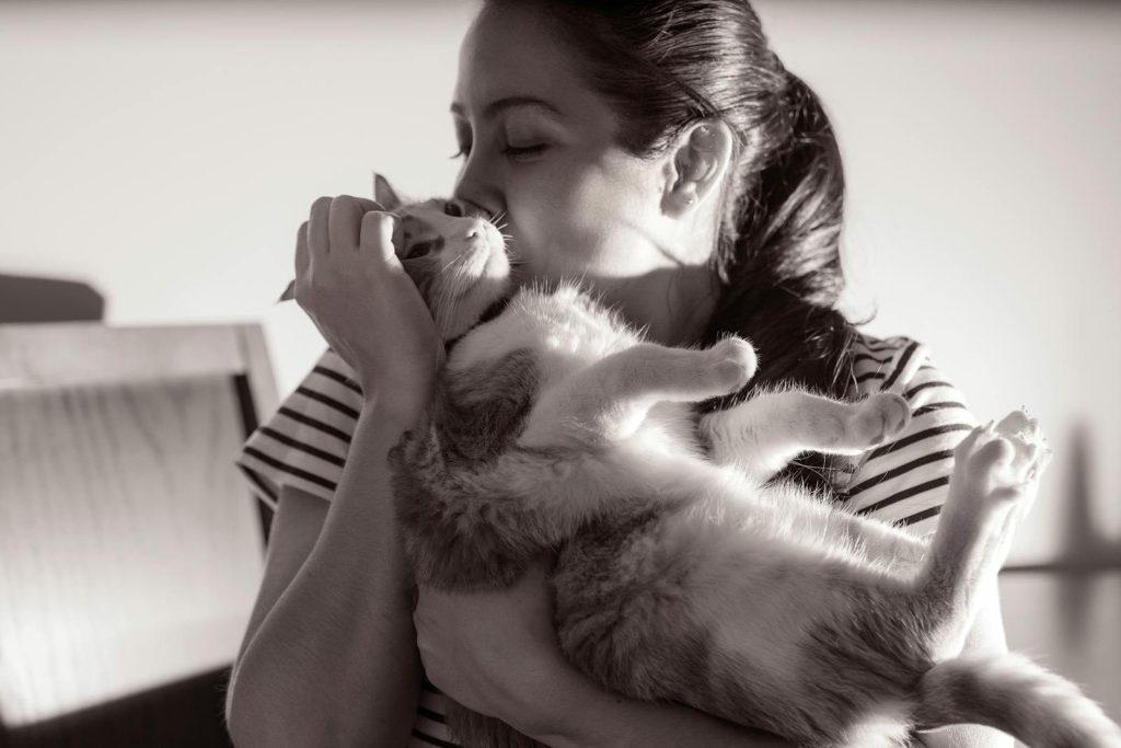 A woman gently kisses her cat, capturing a tender moment in black and white.