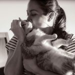 A woman gently kisses her cat, capturing a tender moment in black and white.