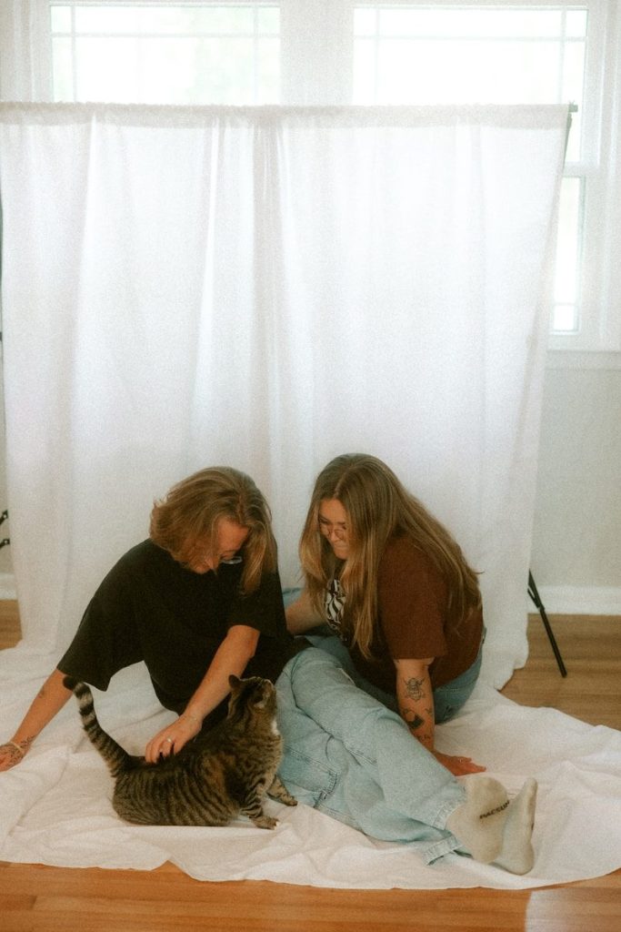 Two women pet a cat in front of a white backdrop.