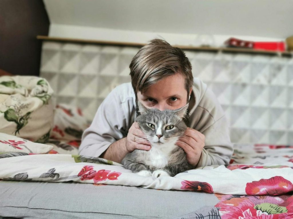 Man chilling with his grey tabby cat on a colorful bed. Cozy and peaceful moment.