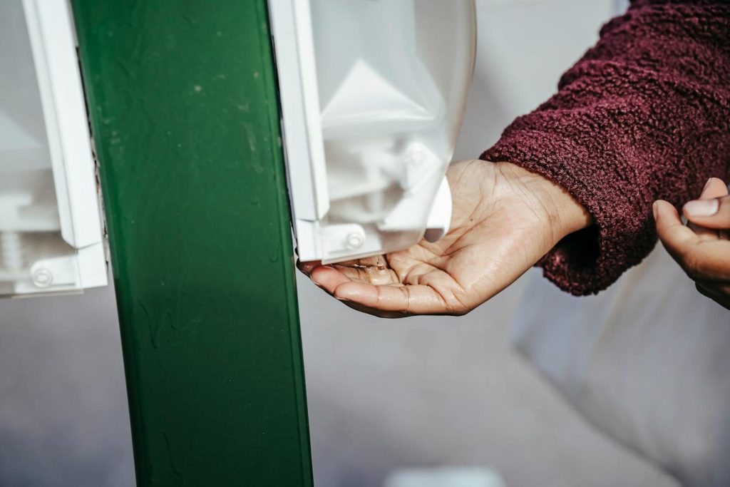 Crop anonymous black female in warm coat standing in street and using sanitizer in daylight
