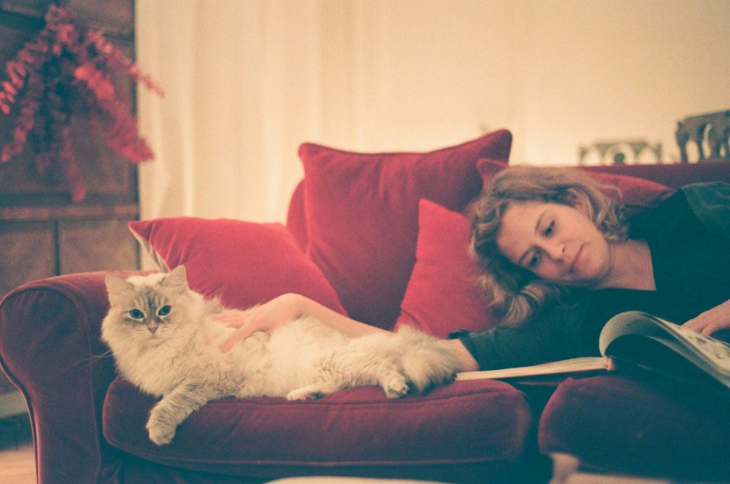 a woman reading a book while laying on a couch with a cat