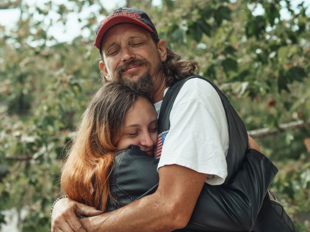 A father and daughter share a warm embrace in a green outdoor setting, radiating happiness and love.