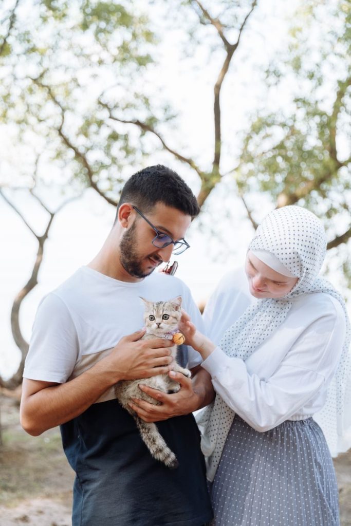A smiling couple lovingly holds a kitten outdoors, showcasing affection and warmth.
