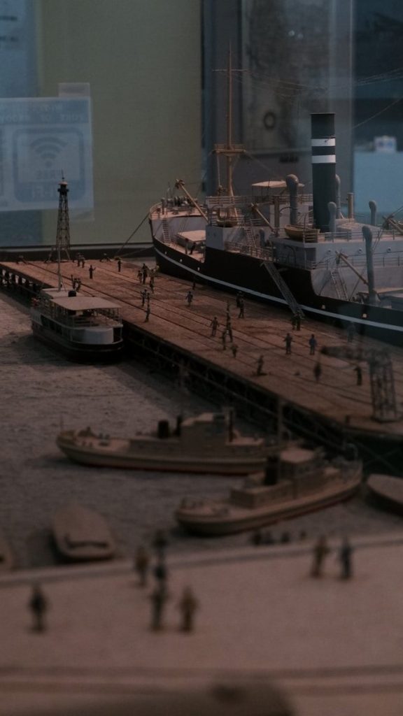 Model ships docked at a pier with tiny figures.