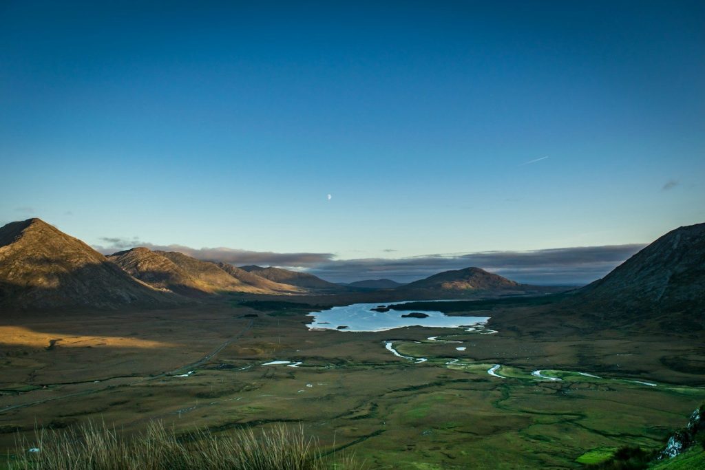 Vast mountain valley with a serene lake at sunrise.
