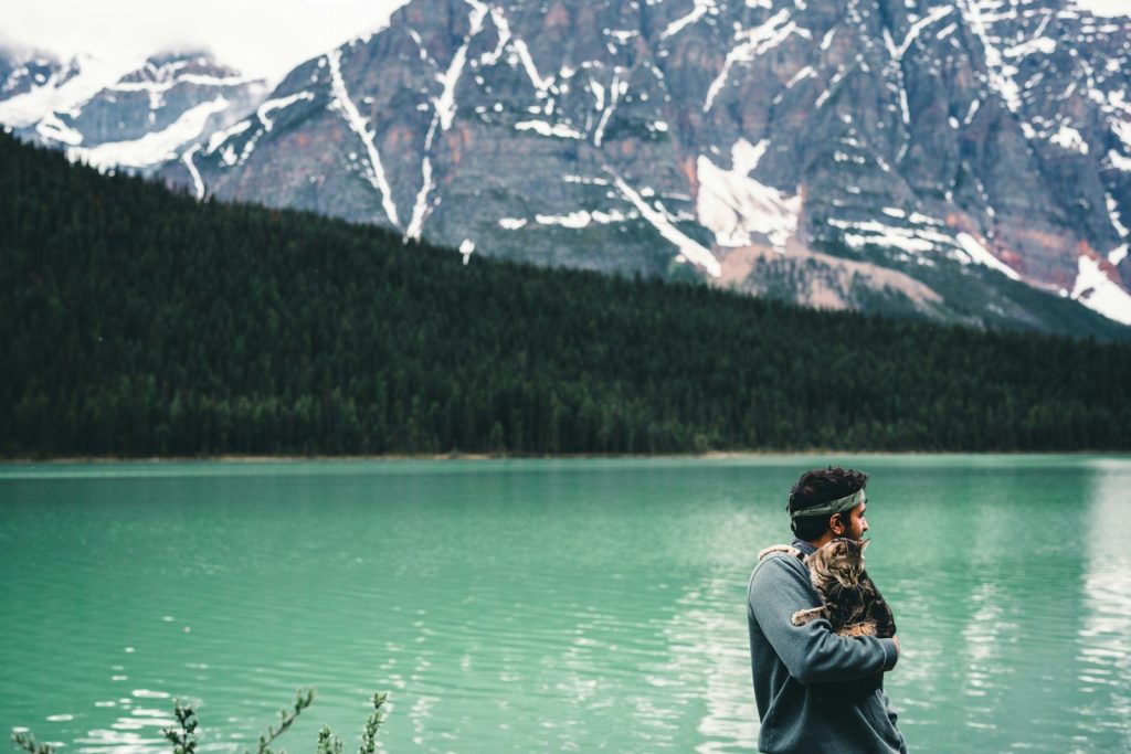 a man standing next to a lake with mountains in the background