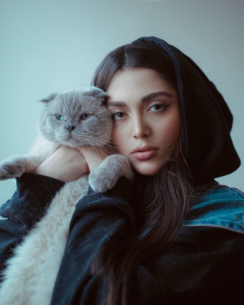 A close-up portrait of a woman holding a British Shorthair cat, both gazing at the camera.