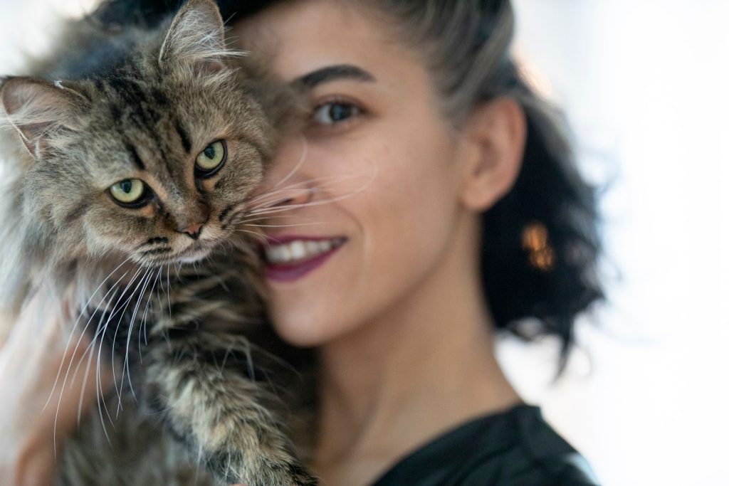Close-up of a woman lovingly holding a fluffy tabby cat indoors.