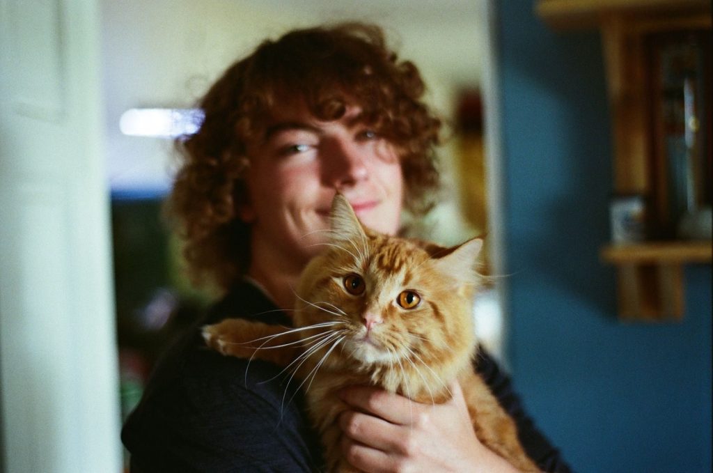 A young man with curly hair holding a fluffy orange tabby cat in a cozy indoor setting.