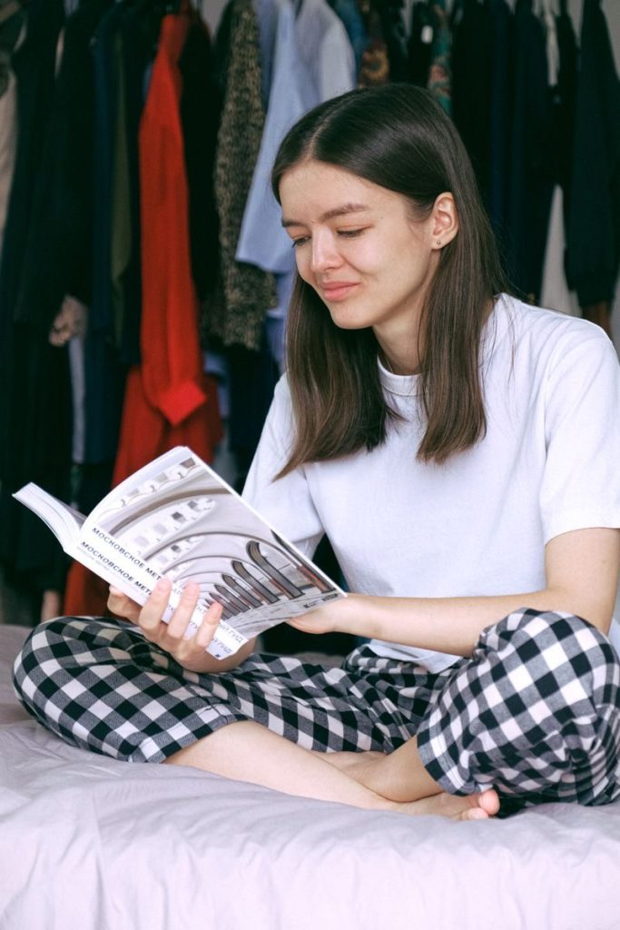 Woman enjoying a peaceful morning reading in a cozy bedroom, dressed in casual pajamas.