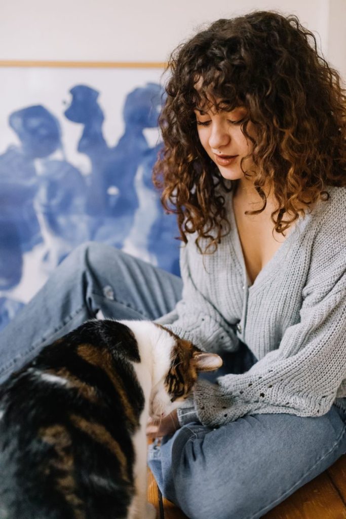 A woman with curly hair gently petting a cat indoors, exuding warmth and coziness.