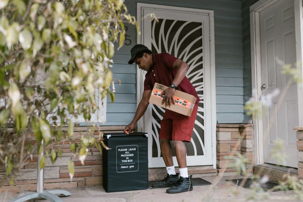 A courier delivering a package to a porch, placing it in a designated box.