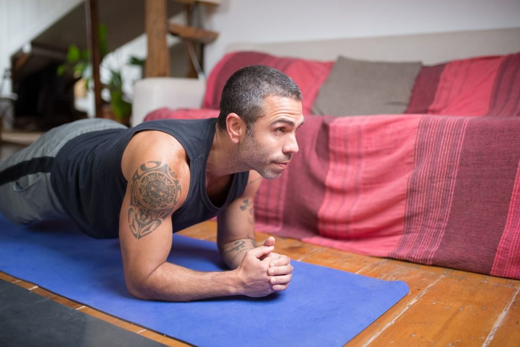 Man doing plank exercise indoors on a yoga mat, embracing a healthy lifestyle.