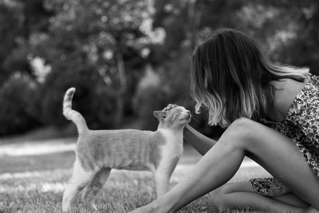 A black and white photo of a woman lovingly petting a cat outdoors, showcasing a calm moment.