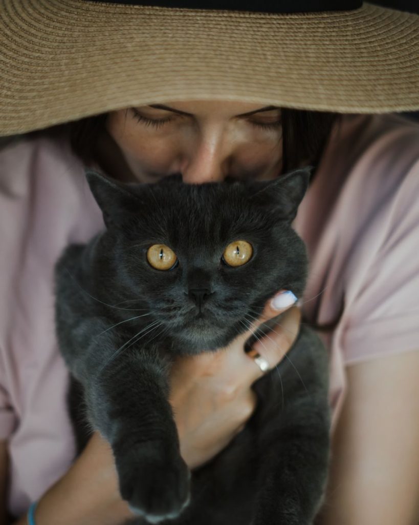A woman in a hat lovingly holds a British Shorthair cat, showcasing a tender human-animal bond.