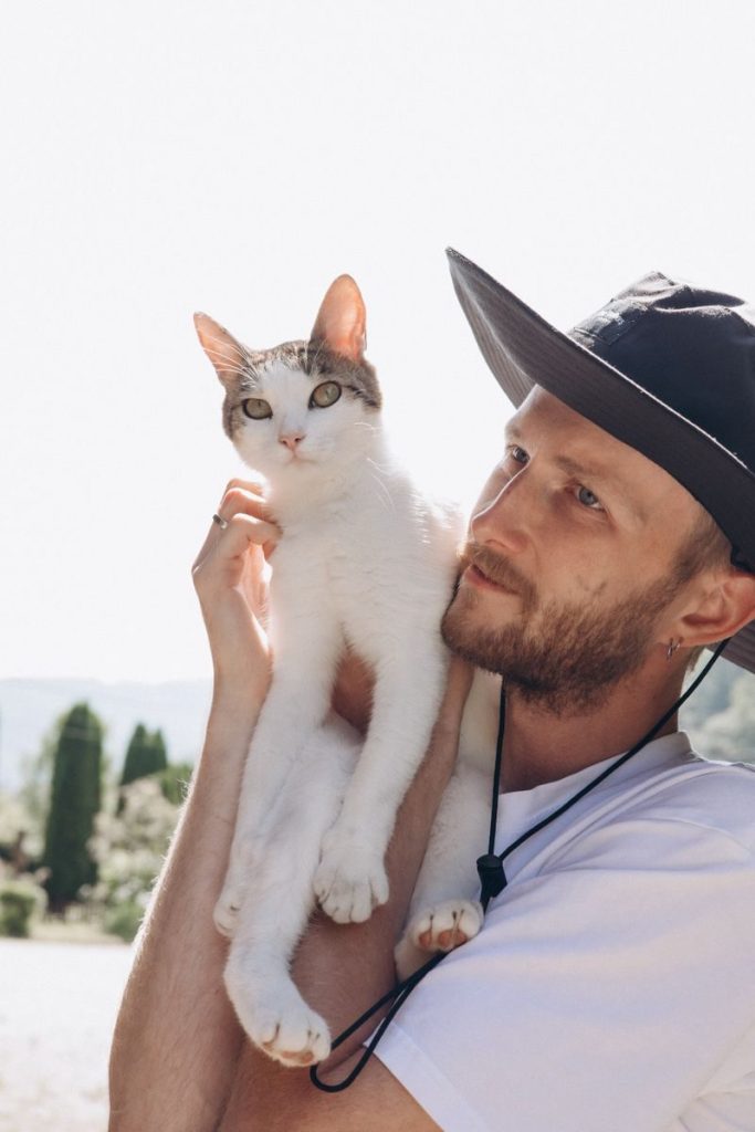 Man holding a white and tabby cat in a sunny outdoor setting, showcasing leisure and companionship.