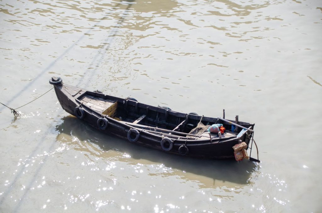 A solitary traditional wooden boat floats on a calm river under bright sunlight.