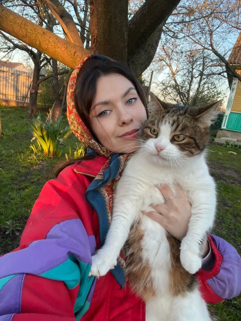 Woman in colorful jacket outdoors holding a tabby cat during springtime.