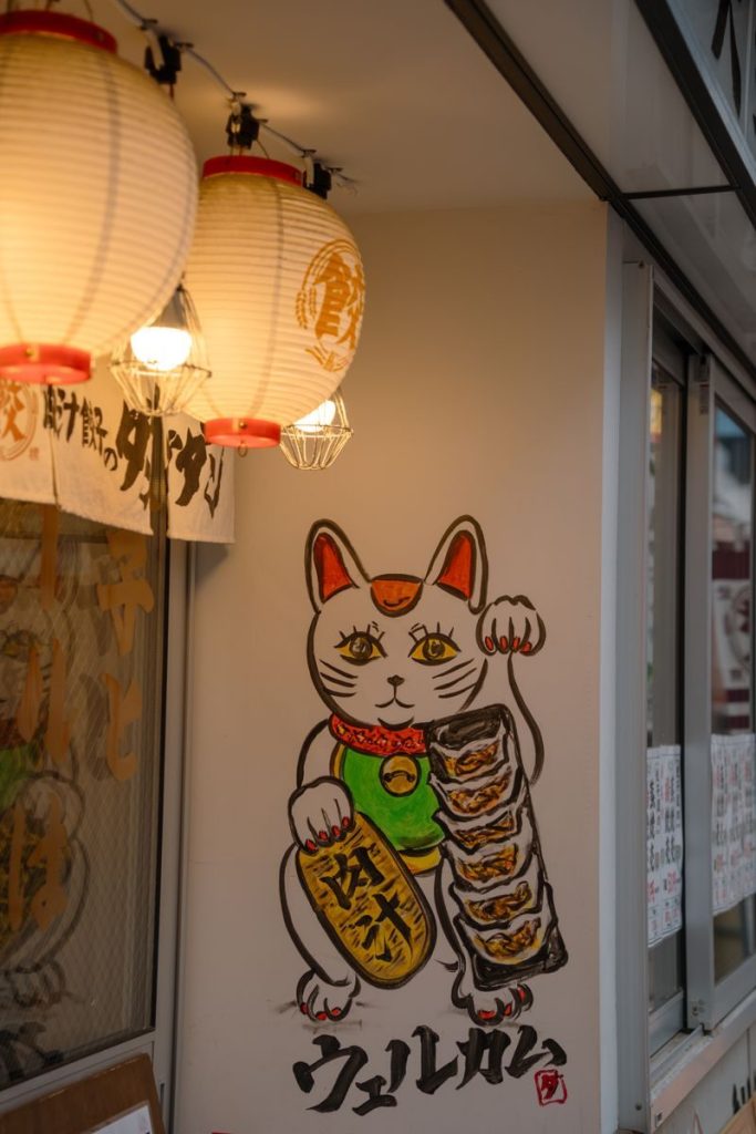 Traditional Japanese Maneki-neko mural with lanterns in Tokyo street scene.