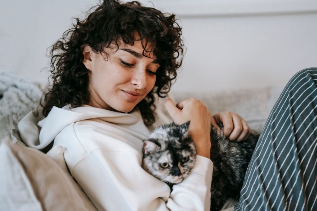 Side view of adult content female cuddling and caressing cute cat while resting on soft couch at home